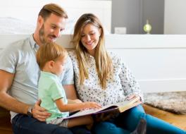 A mother and father sitting with their young son and reading a book