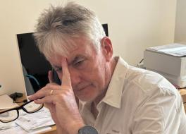 A man looking defeated, with a phone to his ear and his other hand holding a pair of glasses and touching his forehead