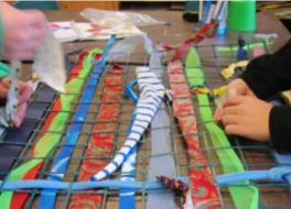 Two pairs of hands creating a mesh-style piece of art, involving strips of fabric and thread