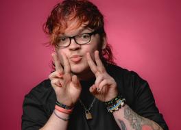 A man wearing glasses, doing two peace signs with his hands and pouting