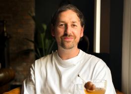A man sitting at a restaurant table and smiling, with two drinks on the table