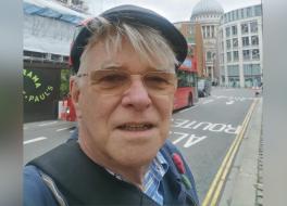 A man with a London street as a backdrop, smiling