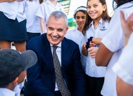 A man in a suit, smiling, surrounded by schoolchildren