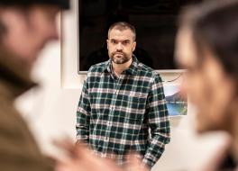 A man standing looking at the camera, with two people in front of him, out of focus