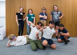 Eight children smiling, some standing, some kneeling and one lying down.