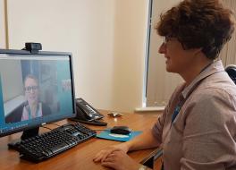 A woman sitting at a desk in an office looking at a computer screen while having a video call