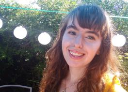 A woman in garden with lights behind her head, smiling for the camera