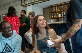 A young man and woman in a cafe looking at a waitress and holding a mobile phone to a card reader