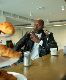 A man at a coffee shop counter talking to a woman obscured by a display of croissants