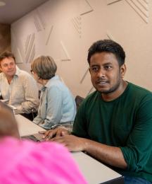 A man sitting at a desk speaking to a woman sitting opposite, whose face we can't see
