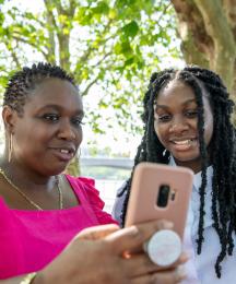 A mother with her daughter, both looking at a phone the mother is holding