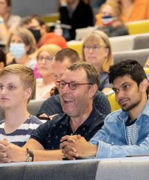 Three men sitting in a lecture theatre, looking to the left and laughing