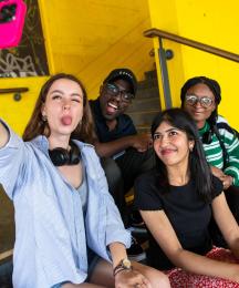 Three women and two men sitting and posing for a selfie photo from a phone held by one of the women
