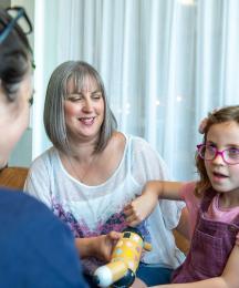 A young girl holding a toy and sitting with her mother while talking to a woman sitting opposite them