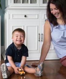 A mother playing with her young son, both sitting on the floor and laughing