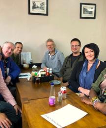 Seven people sitting around a cafe table smiling for the camera