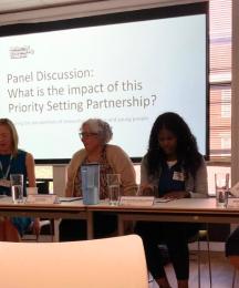 Four women sitting at a desk in front of a powerpoint presentation slide
