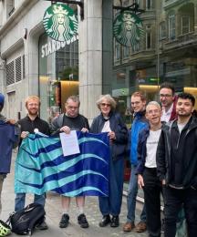A group of people standing outside a coffee shop. Some are holding a flag