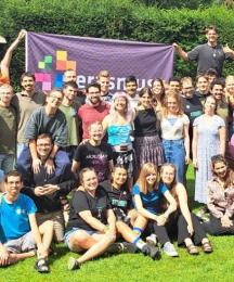 A big group of people, huddled together and smiling, some standing, some sitting and crouching