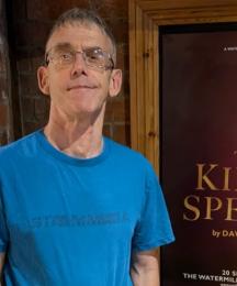 A man smiling in front of a poster with the words 'The King's Speech'