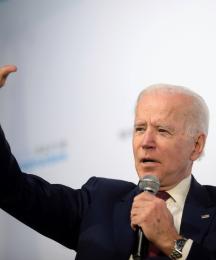 President Joe Biden speaking into a microphone and waving