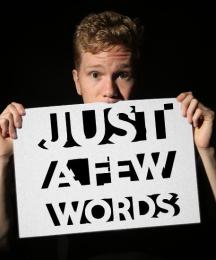 A man holding a sign up to cover his mouth. The sign reads 'Just a few words'