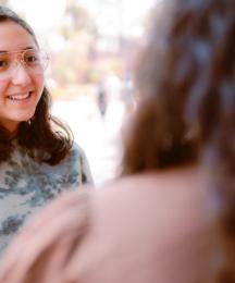 A young woman in conversation with somebody who has their back to us.