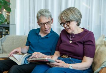 A man and a woman sitting next to each and looking at a tablet the woman is holding