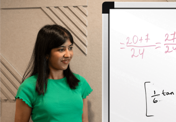 A woman holding a pen and standing beside a whiteboard which has writing on it