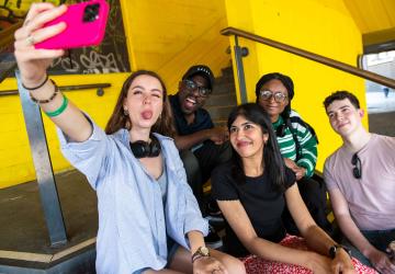 Three women and two men sitting and posing for a selfie photo from a phone held by one of the women