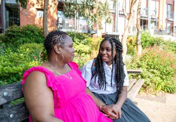 A mother sitting with her daughter on a park bench and chatting
