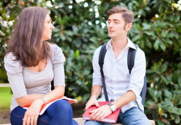 A young man wearing a backpack sitting on a bench talking with a woman