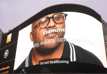 An advertising screen in Piccadilly Circus displaying a man looking at the camera, with the words 'Stamma' on it