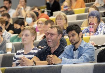 Three people sitting in a lecture theatre and smiling at something off camera