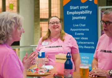 A woman smiling, with two people in front of her chatting