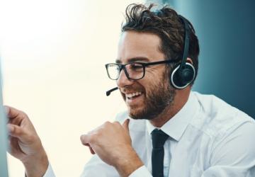 A man in a call centre wearing a phone headset and smiling