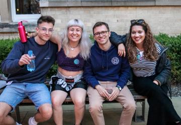 Group of four people sat on a bench drinking water and smiling