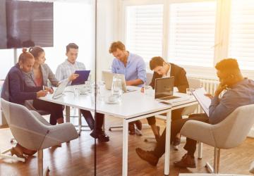 A group of people sitting round a table in a work setting, each one looking at laptops or tablets