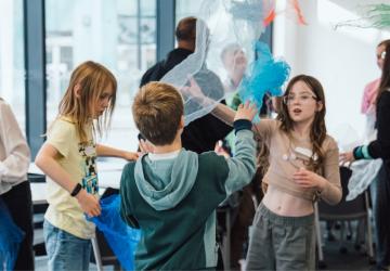 Three children playing with pieces of fabric, waving them through the air