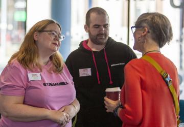 A woman speaking to another woman who is listening. A man stands in the background