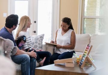 A father and mother sitting on a sofa with a young daughter between them, siting opposite a therapist who is taking notes