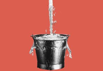 A bucket, with water pouring into it and spilling over the sides
