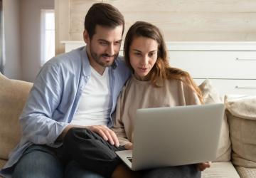 A man and a woman sitting on a sofa looking at a laptop computer