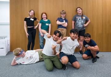 Eight children smiling, some standing, some kneeling and one lying down.