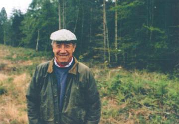 A man standing in front of a woodland, looking at the camera and smiling