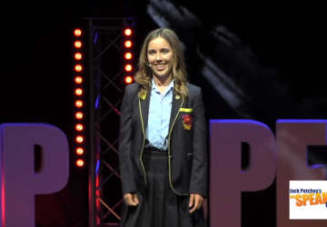 A teenage girl in a school uniform with a microphone smiling