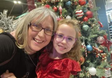 A woman and her young daughter looking at the camera and smiling, with a Christmas tree in the background.