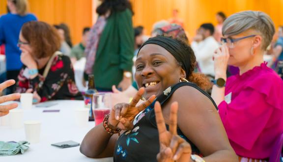 Woman smiling with peace signs sat at a conference dining table
