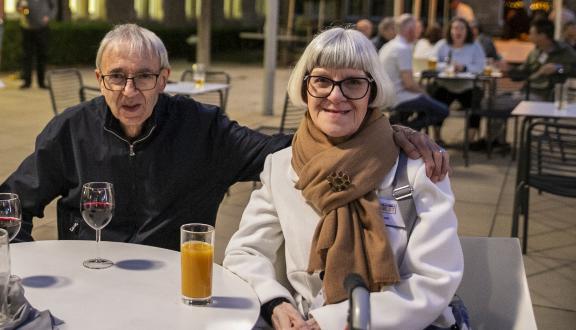 An older man and woman smiling while sat at a table outside the conference venue