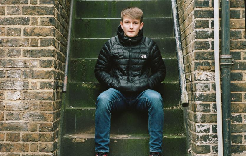 Teenage boy sitting on steps, looking intently at camera, hands in pockets